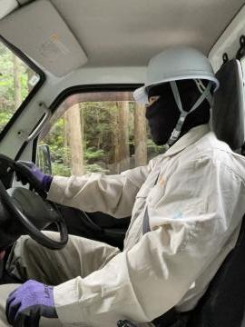白いヘルメットと作業服と紫色の手袋を着用した職員が運転席で車を運転している