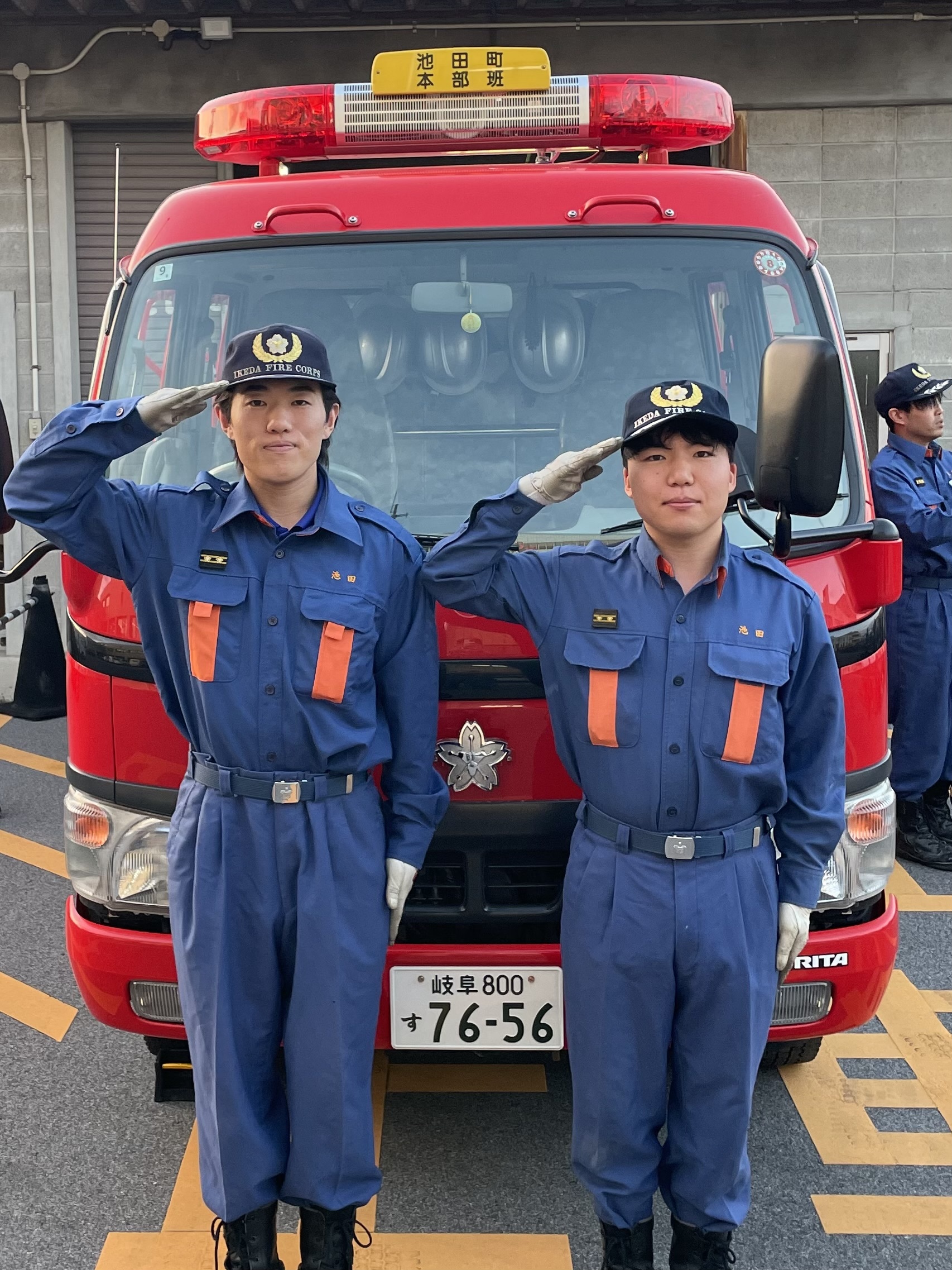 消防車の前に並んで敬礼する青い制服と帽子を着用した職員